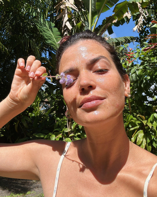 Woman wearing face mask holds flower up to her eye