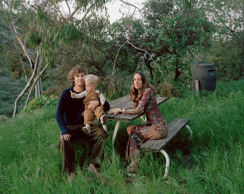 Man, woman and child sitting on a picnic table amongst long grass and trees