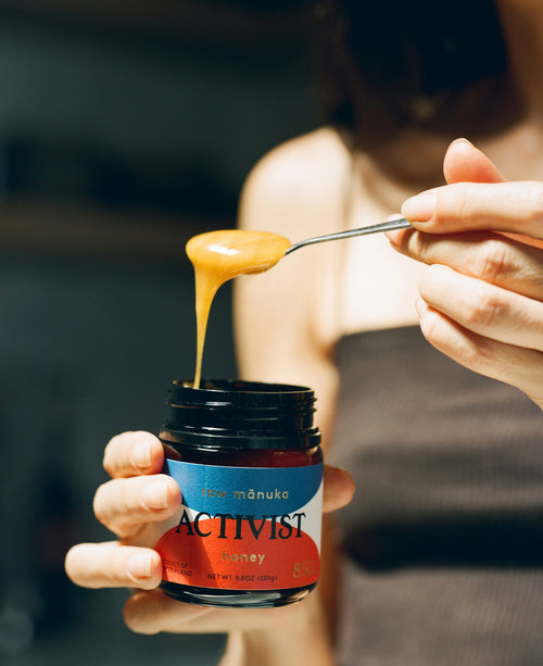 a person holding a jar of ACTIVIST Manuka honey and a spoon